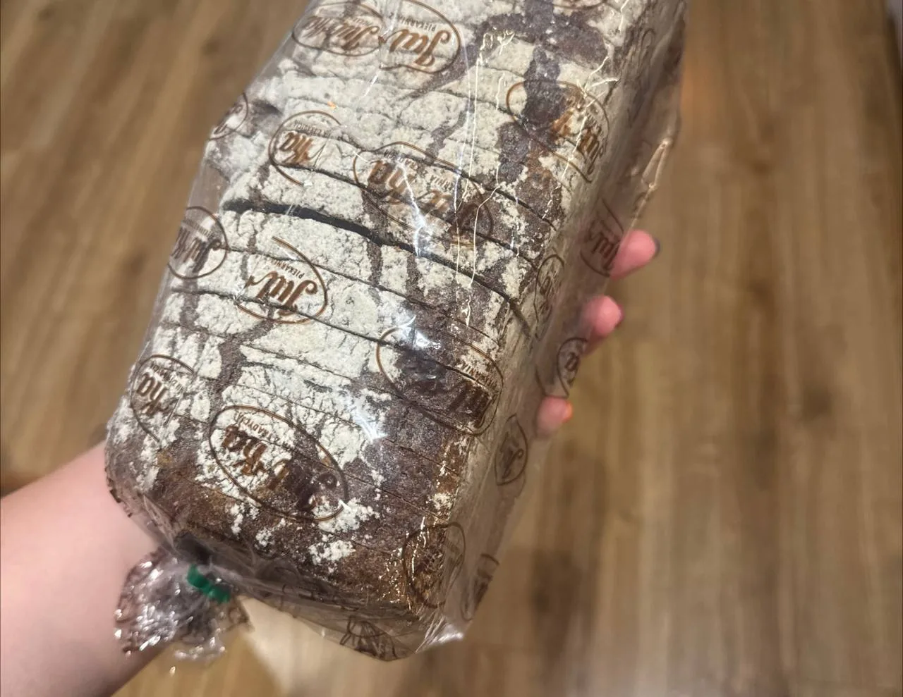 Рука тримає буханець хліба в прозорій упаковці на фоні дерев’яної підлоги