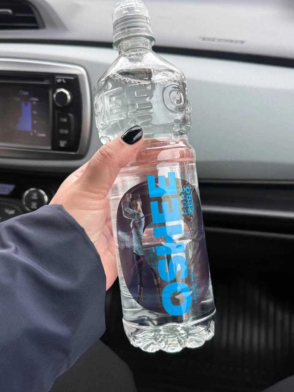 Рука з пляшкою води в салоні автомобіля, крупний план на фоні панелі приладів