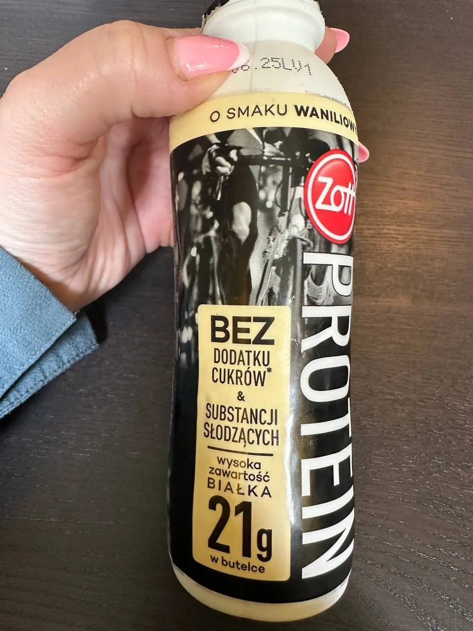 Рука тримає пляшку протеїнового напою з польським написом без доданого цукру на дерев’яній поверхні