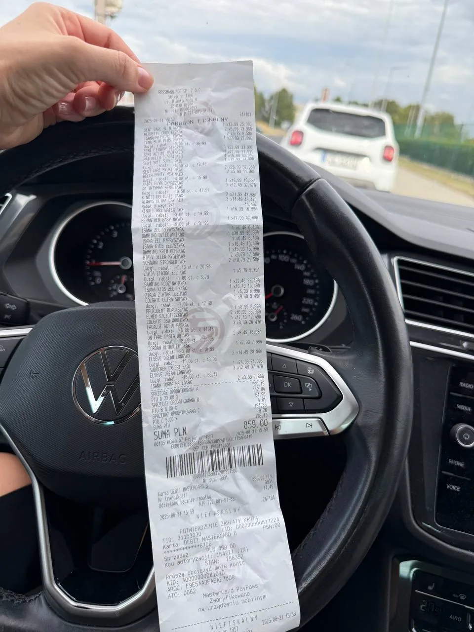 Людина в салоні авто тримає довгий чек над кермом, натякаючи на часті покупки їжі та поступовий набір ваги